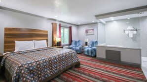Quarto de hotel com uma cama grande, chuveiro, duas poltronas e um tapete vermelho estampado.
