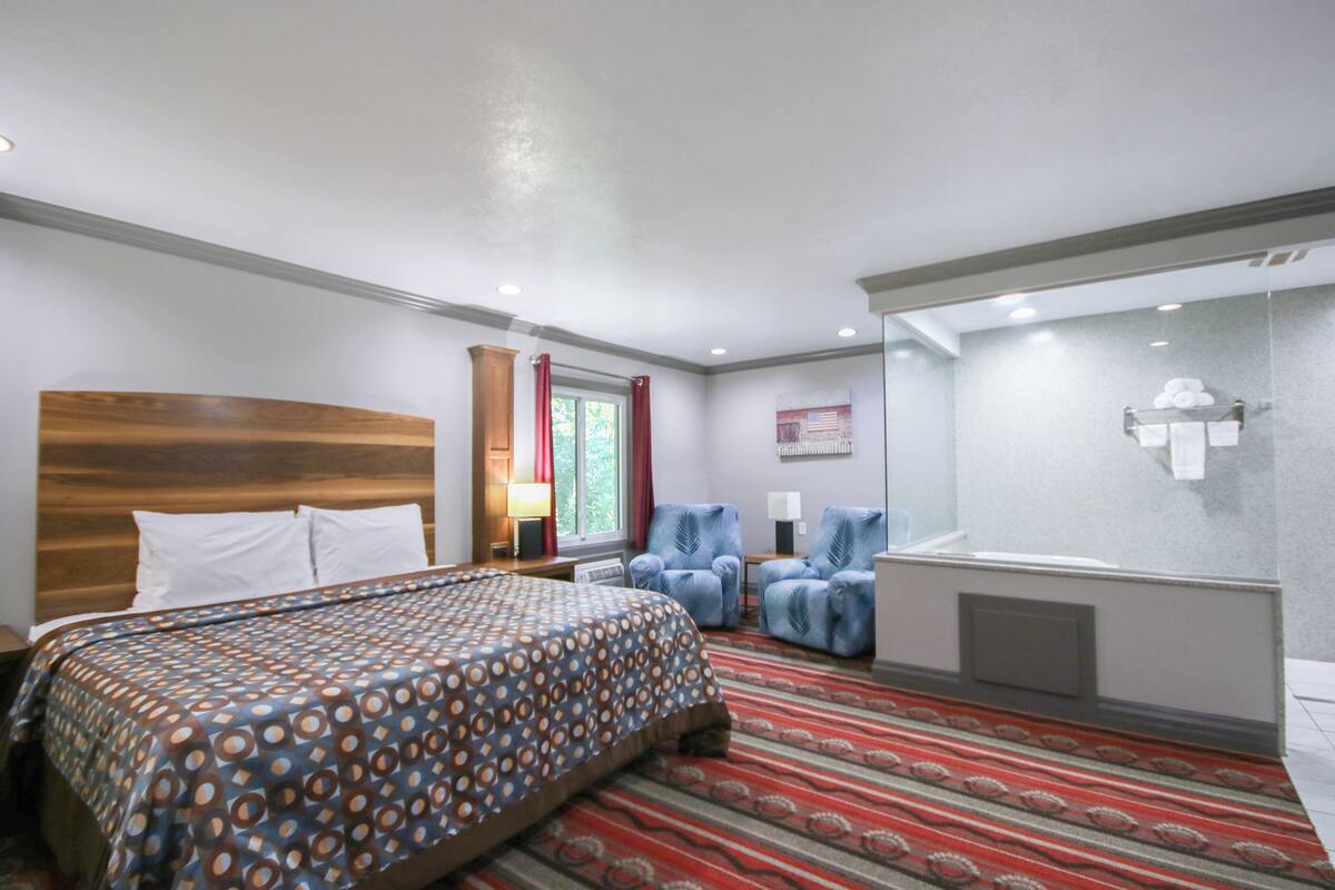 Hotellihuone, jossa on suuri sänky, suihku, kaksi nojatuolia ja punakuvioinen matto.