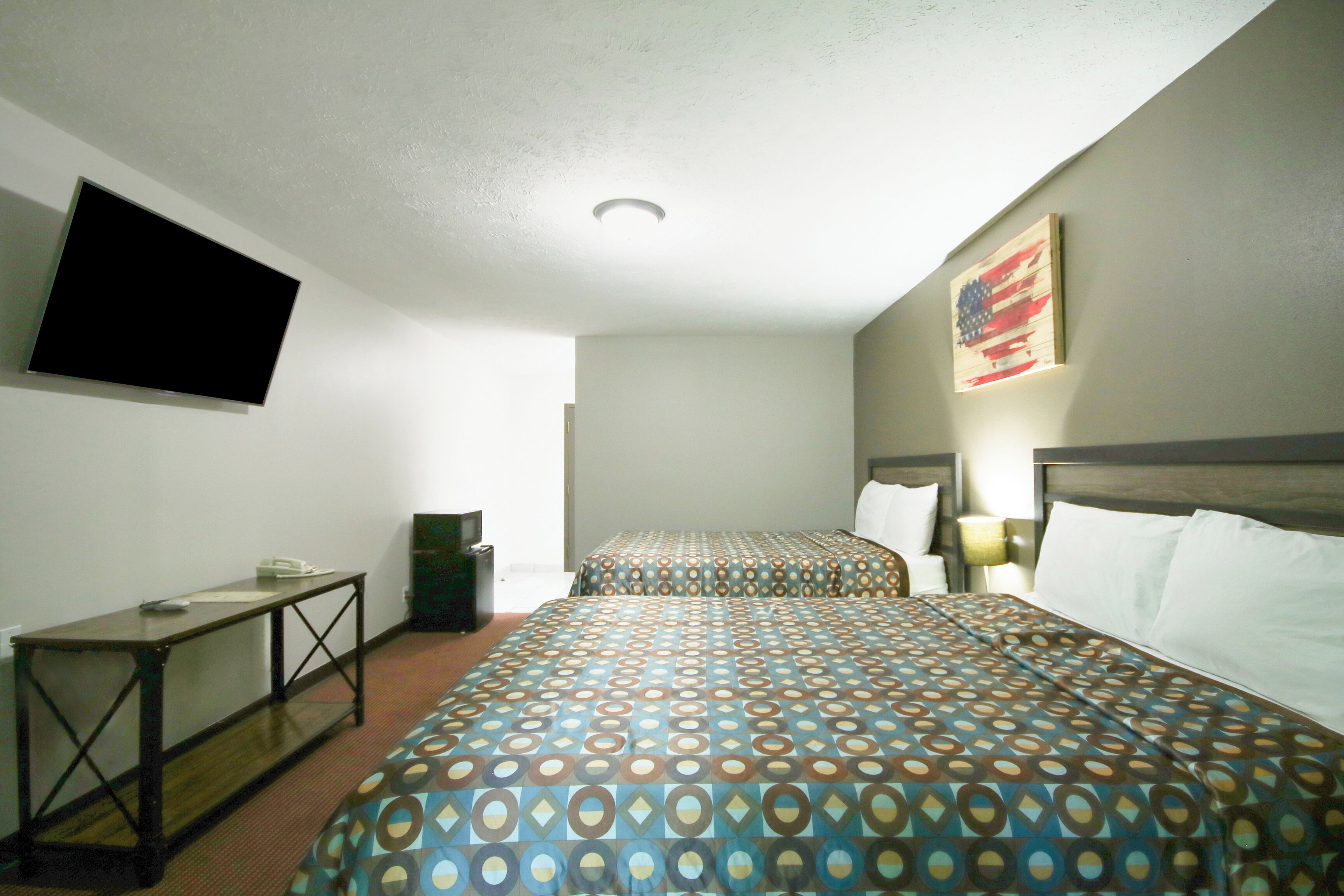 A hotel room with two beds, a TV mounted on the wall, a desk, and a painting.