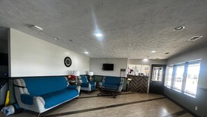 Uma área de recepção com um sofá azul, uma mesa de centro e uma televisão fixada na parede.