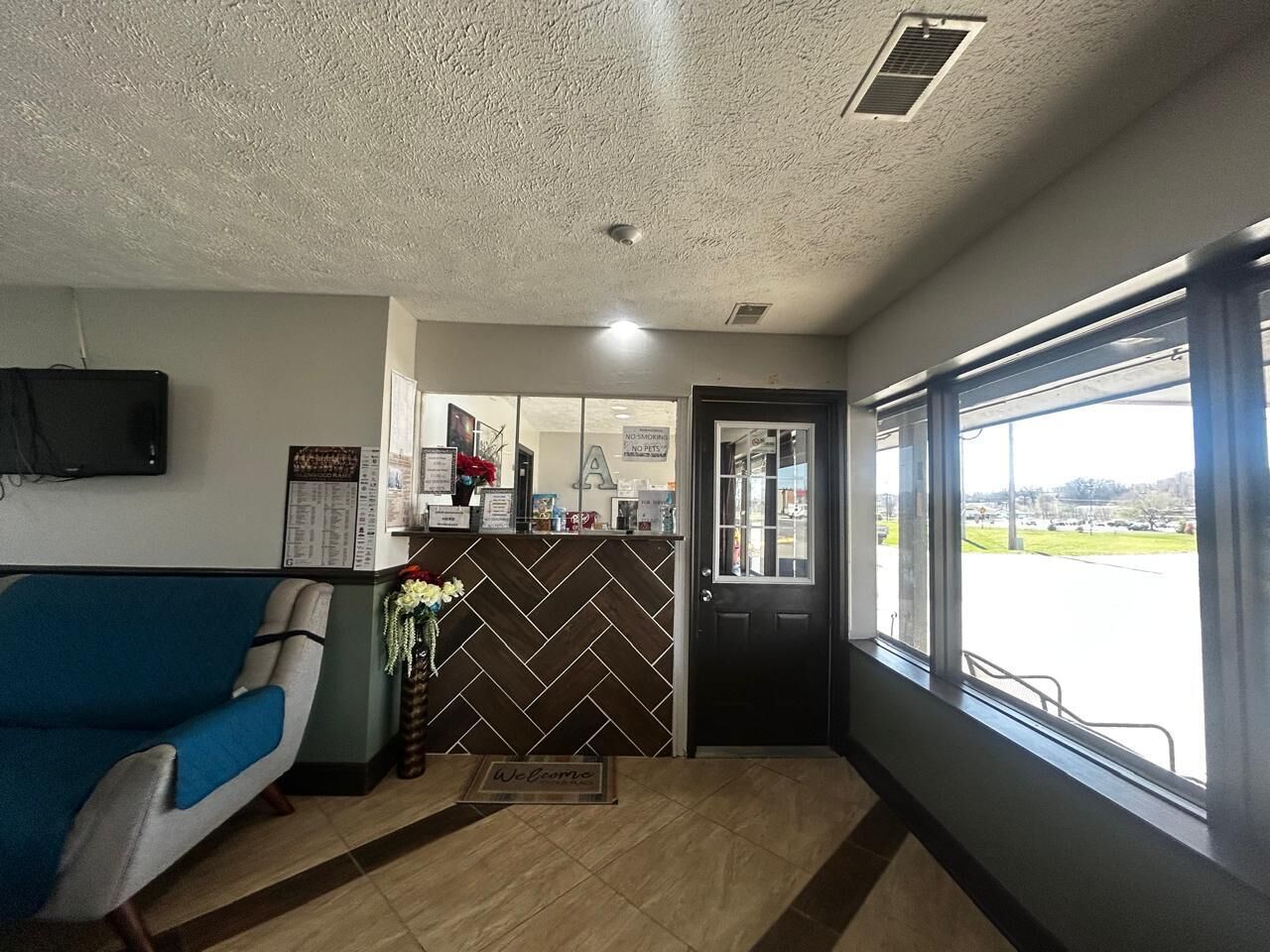 Zona de recepción con un sofá azul, mostrador de recepción, una puerta y una ventana con vista a un estacionamiento.