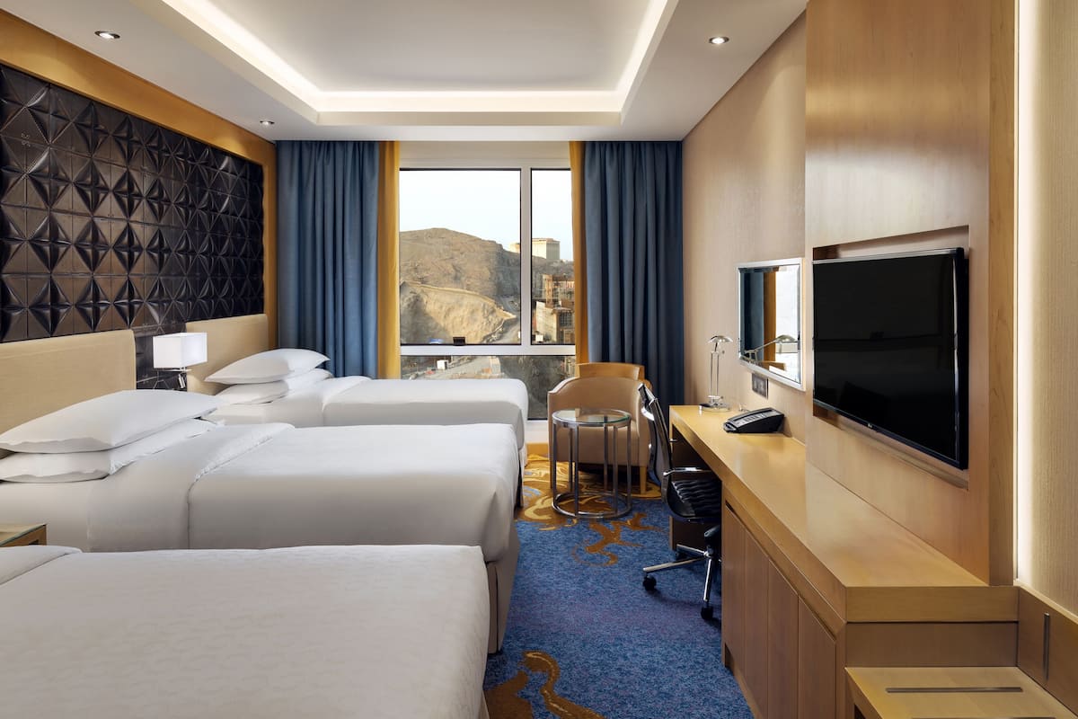 Habitación de hotel con dos camas, un escritorio con televisor, una silla y vistas a un paisaje montañoso.