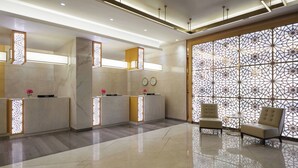 Un área de recepción moderna con mostradores de mármol, una pared decorativa con patrones geométricos y un espacio de estar con dos sillones.