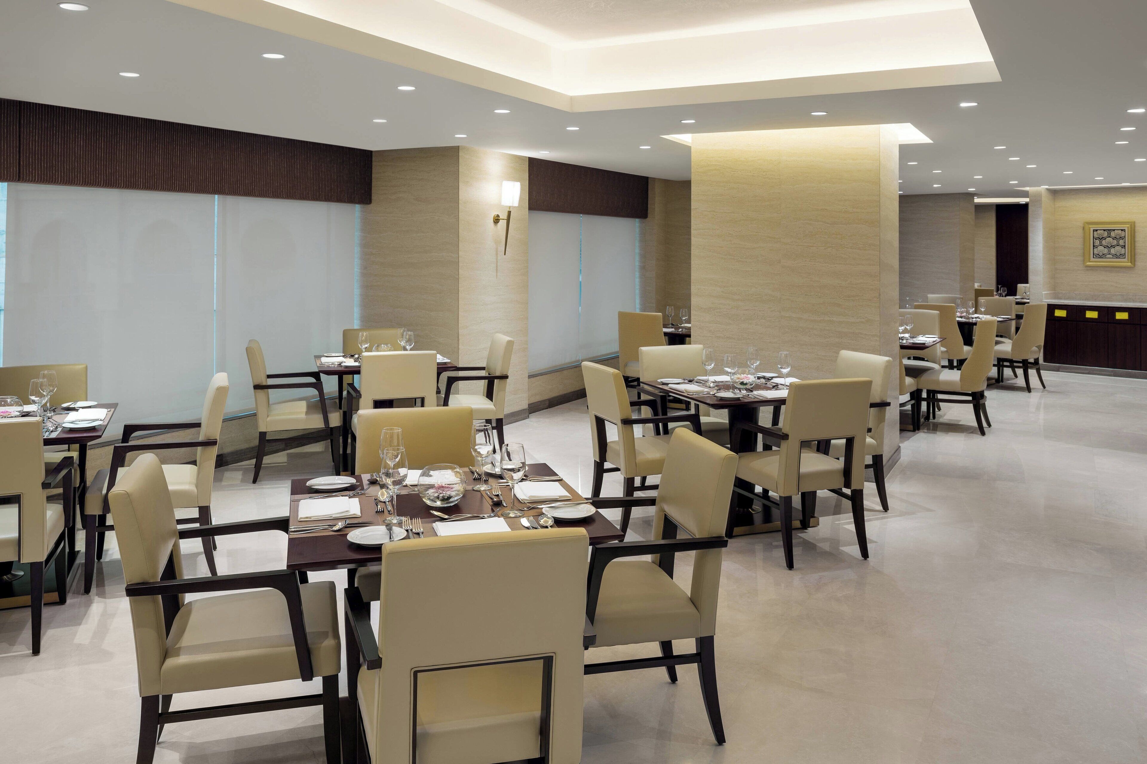 A spacious dining area with multiple tables and chairs, well-lit by ceiling lights, and featuring a modern design with neutral color tones.