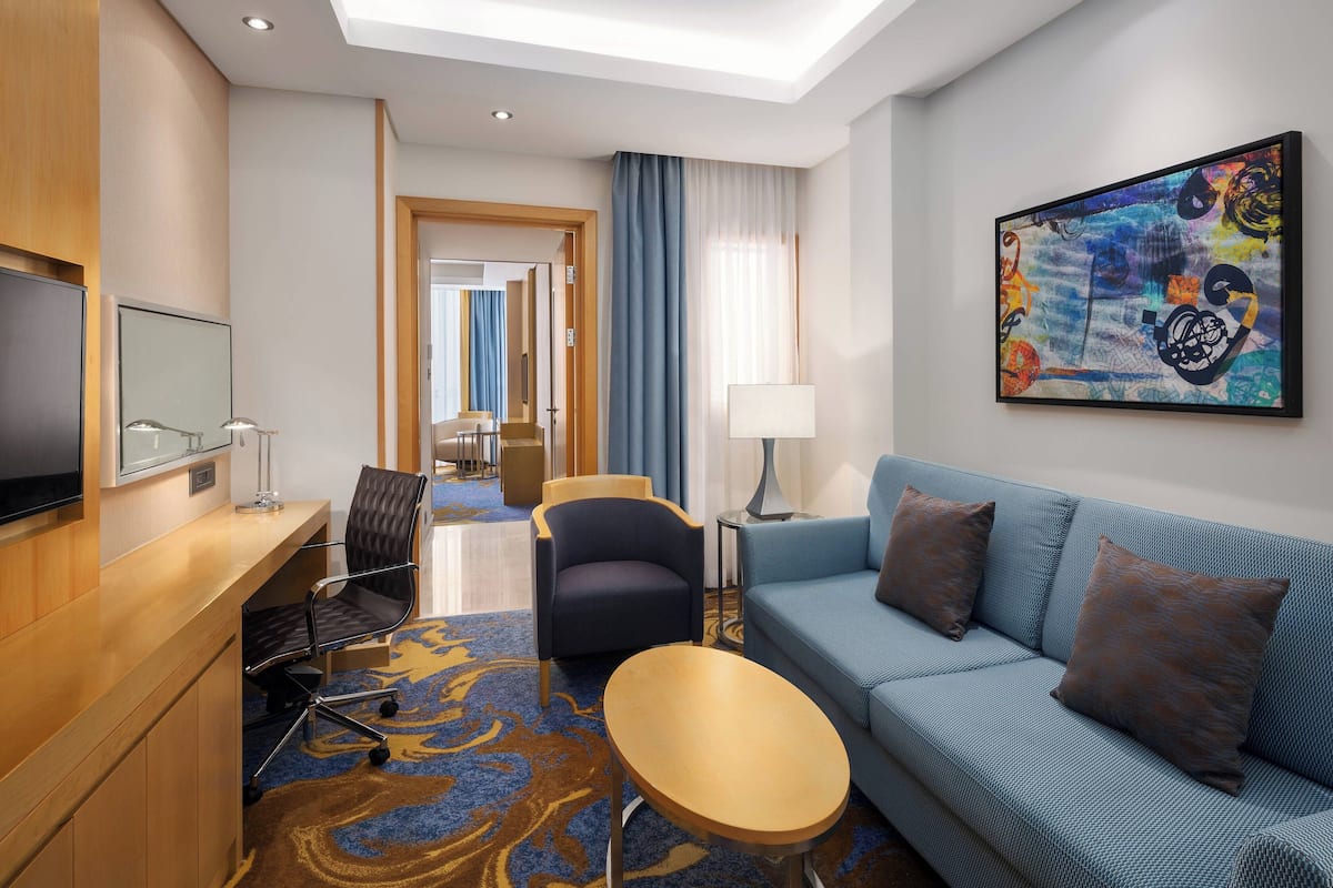 Una habitación de hotel con sofá, sillón, escritorio y un cuadro en la pared.