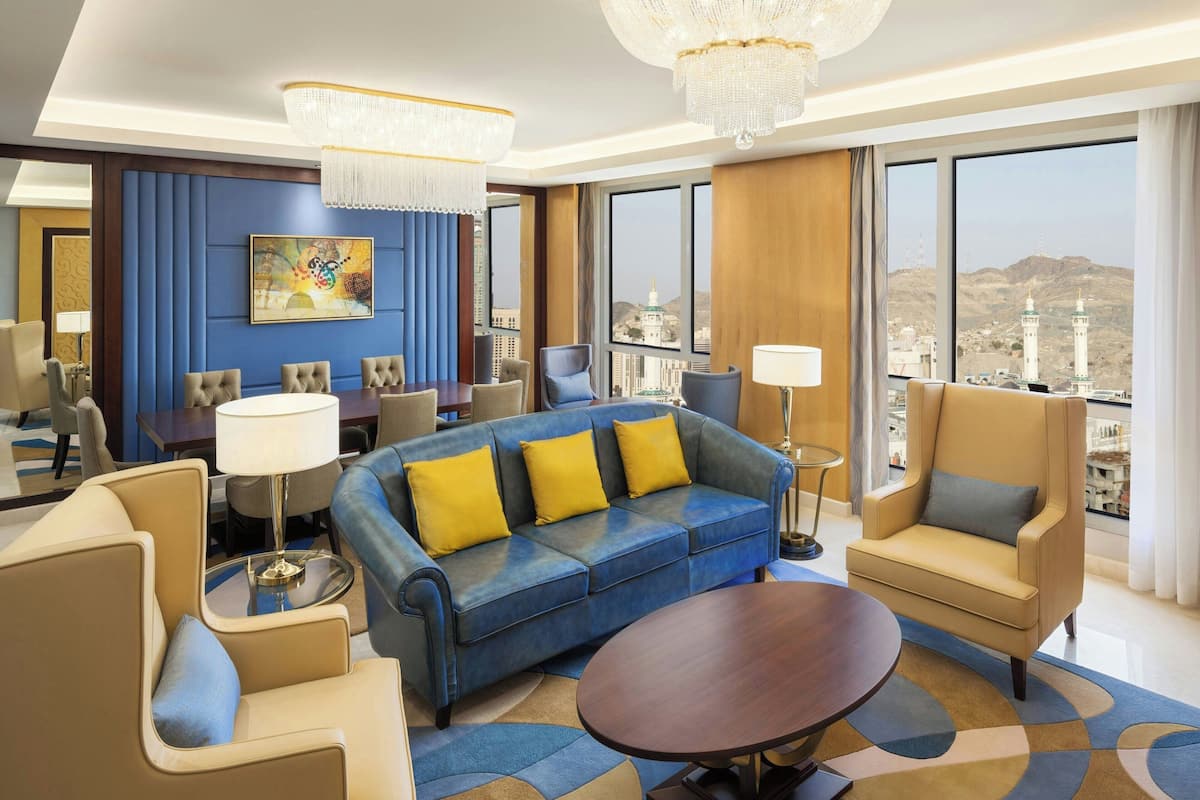 Una habitación de hotel moderna con un ventanal grande, un sofá azul, una mesita de centro redonda y una araña.