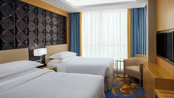 A hotel room with two beds, a TV, a desk, and a window with curtains.