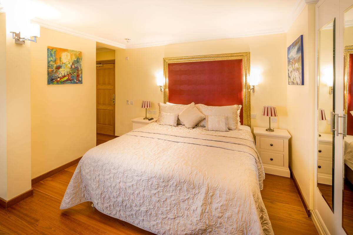 A hotel room with a large bed, two bedside tables, a red headboard, and artwork on the walls.