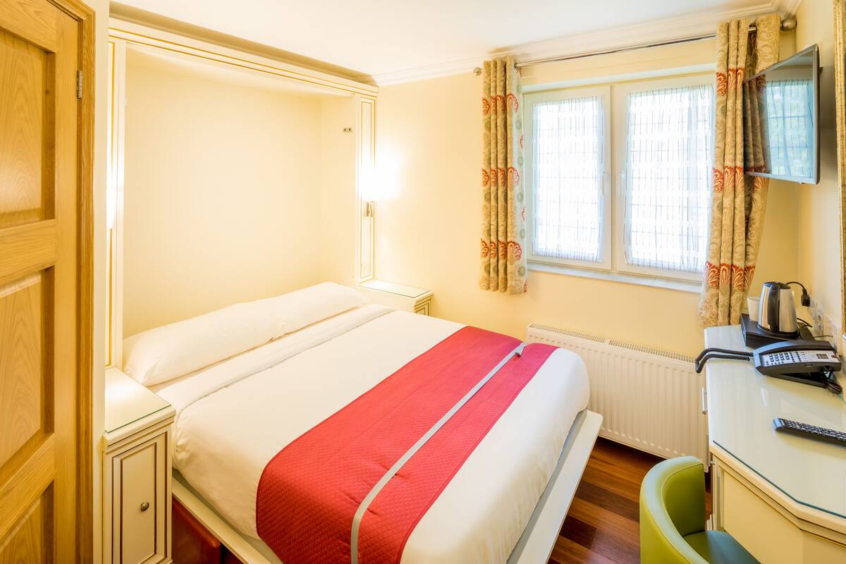 A hotel room with a bed, bedside table, and a desk with a telephone.