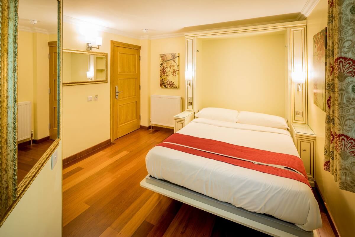 A hotel room with a large bed, a wooden door, a radiator, and a mirror.