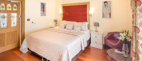 Una habitación de hotel con una cama grande, una mesita de noche, una silla, una pequeña mesa con un jarrón y una puerta con vidrieras.