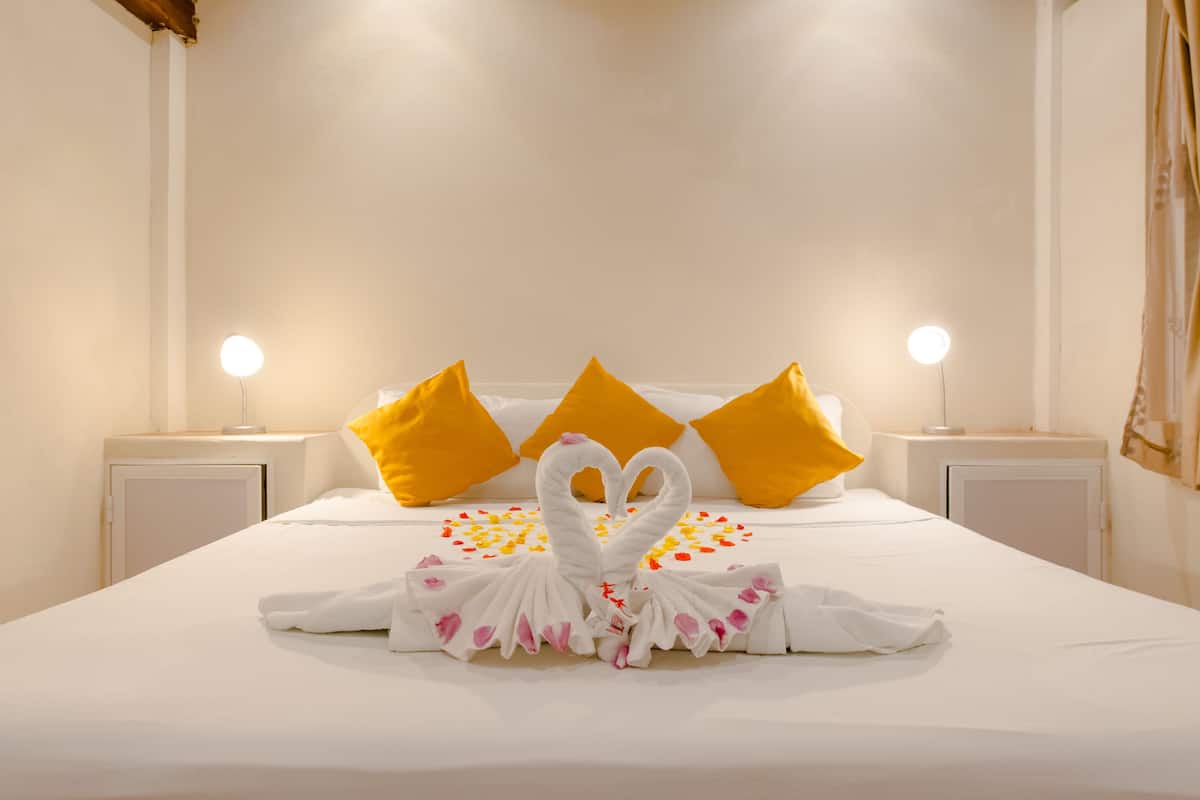 Habitación de hotel con una cama bien hecha, dos lámparas de noche y una toalla con forma de cisne decorativa.