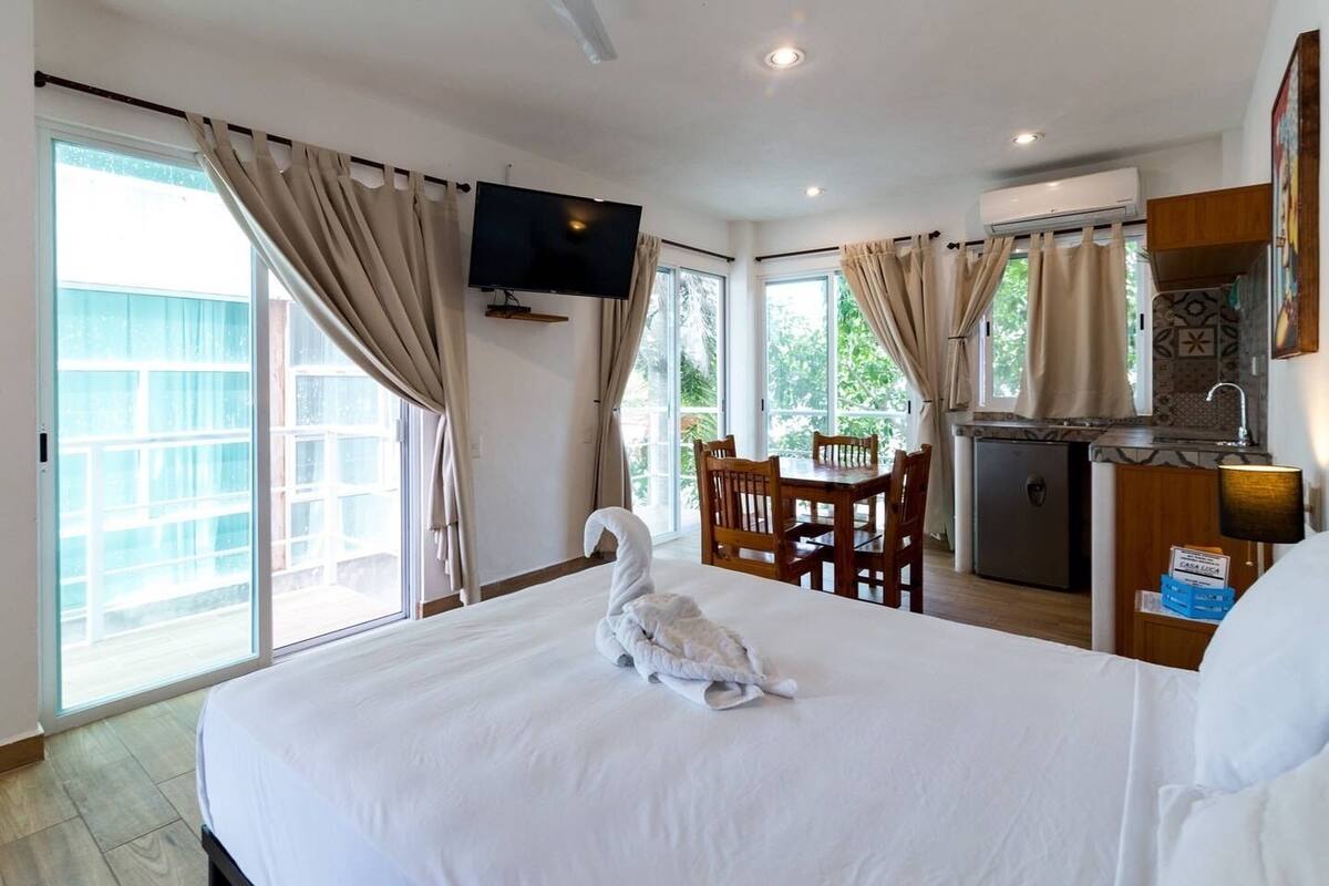 Una habitación de hotel con una cama grande, una mesa de comedor, un televisor y una kitchenette.