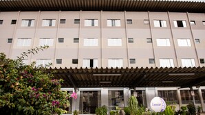 A multi-story hotel with a flat facade, large windows, and a covered entrance area with potted plants and traffic cones. - Hotel Lumiar (Coronel Fabriciano)