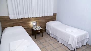 Una habitación de hotel con dos camas individuales, una mesita de noche con lámpara y teléfono.