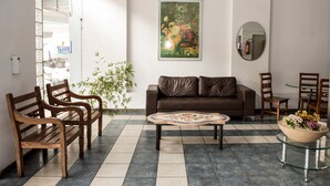A lobby with a brown leather sofa, wooden chairs, a coffee table, a potted plant, and a framed floral painting on the wall. - Hotel Lumiar (Coronel Fabriciano)