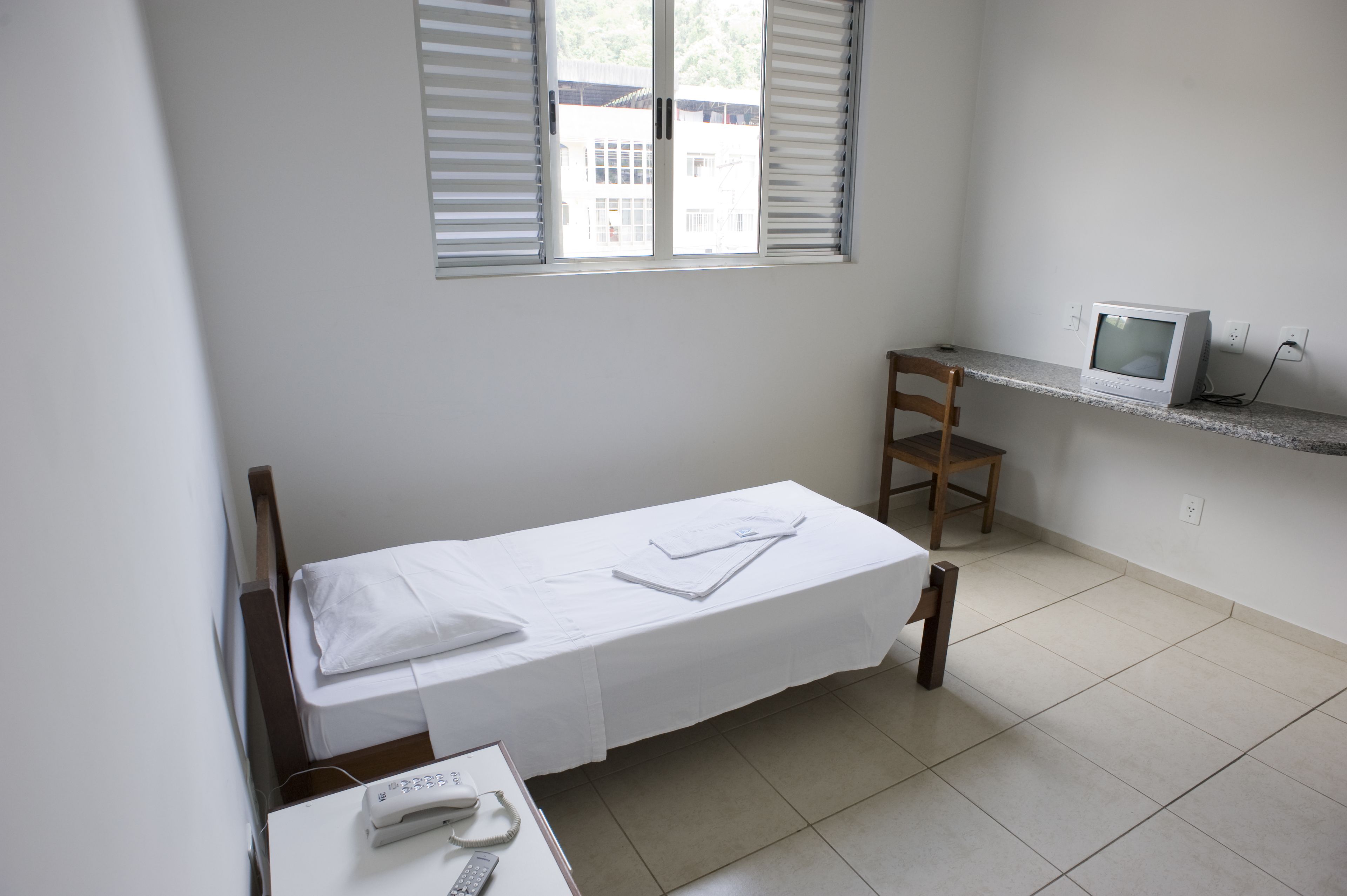 A small, clean room with a single bed, a desk with a computer, and a chair.