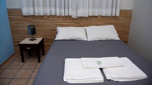 A hotel room with a bed, two pillows, a nightstand with a lamp, and a folded towel on the bed. - Hotel Lumiar (Coronel Fabriciano)