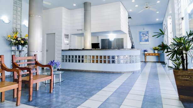 A spacious lobby with a reception desk, wooden chairs, a glass table, and potted plants. - Hotel Lumiar (Coronel Fabriciano)