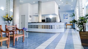 Un vestíbulo amplio con una mesa de recepción, sillas de madera, una mesa de vidrio y plantas en macetas.