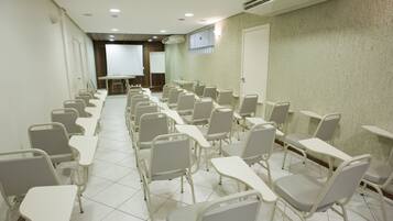 Un salón de conferencias con filas de sillas y mesas, una pizarra y un equipo de aire acondicionado en la pared.