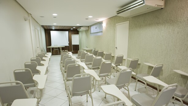 Un salón de conferencias con filas de sillas y mesas, una pizarra y un equipo de aire acondicionado en la pared.