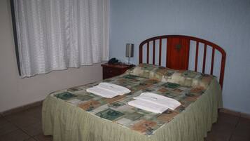 Un dormitori amb llit, una tauleta de nit, una làmpada i una finestra amb cortines.
