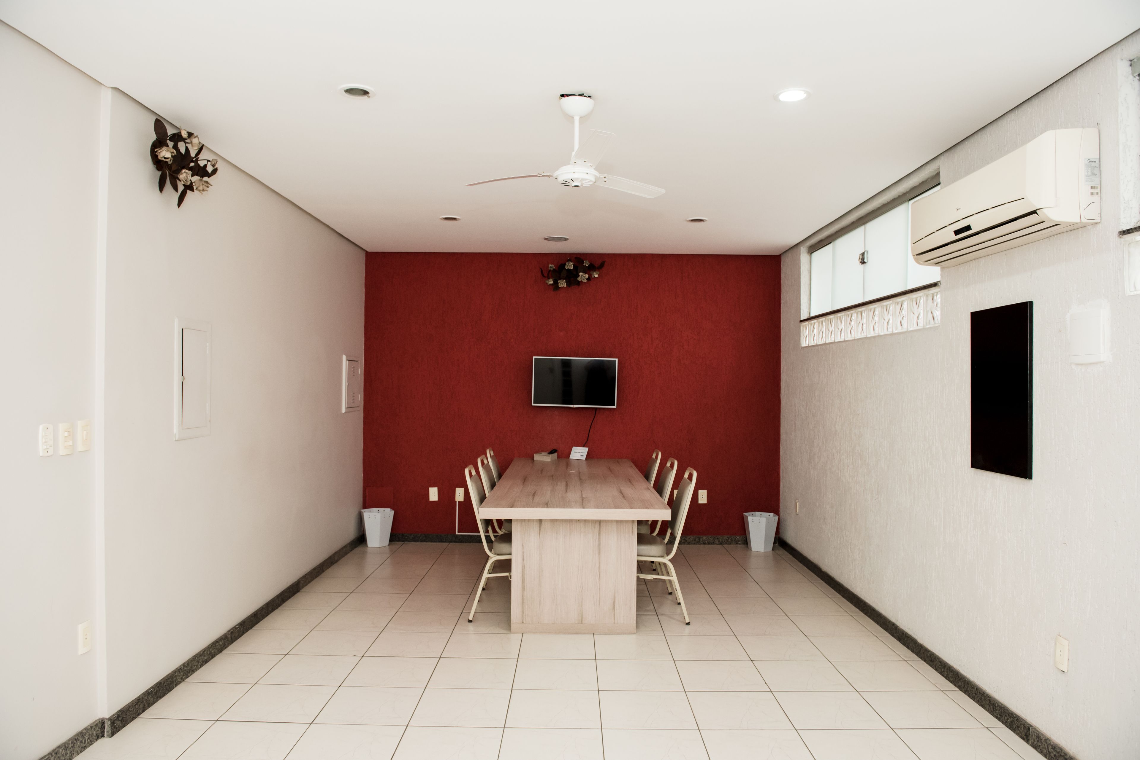 A conference room with a wooden table, chairs, a ceiling fan, a mounted TV, and an air conditioning unit.