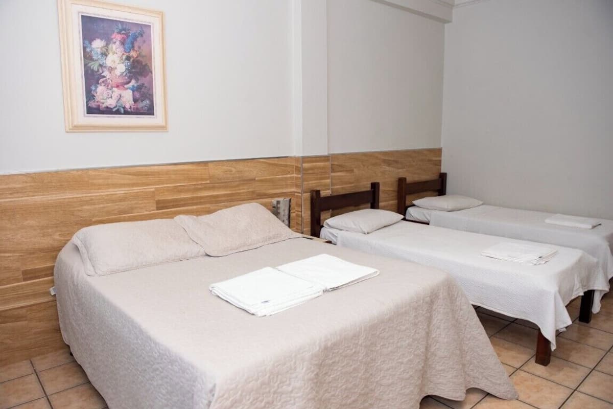 Hotellihuone, jossa on kaksi erillistä sänkyä, puinen pääty, seinällä oleva kehystetty kukka-aiheinen taideteos ja laattalattia.