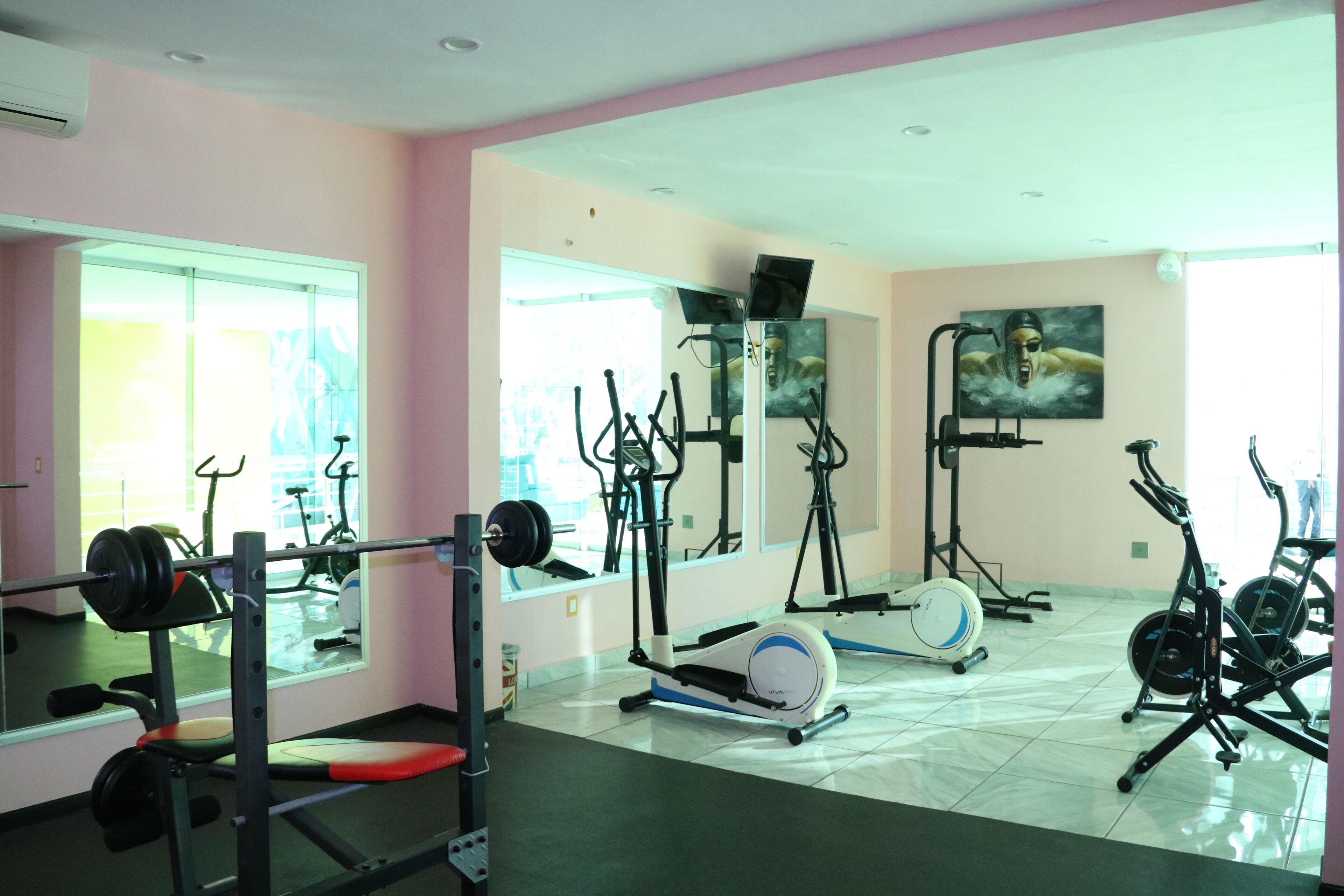 A gym with exercise equipment, a mirror, and large windows.