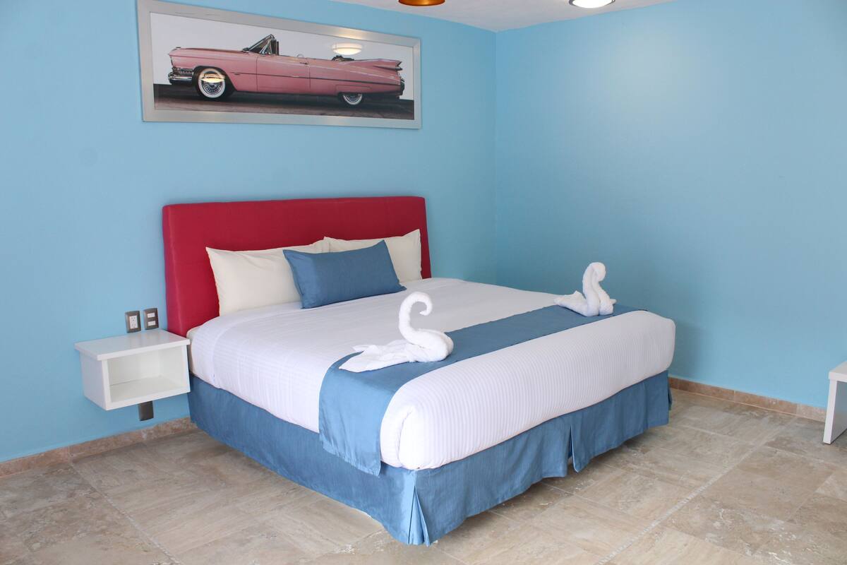 A neatly made bed with a red headboard, white and blue bedding, and a swan-shaped pillow.