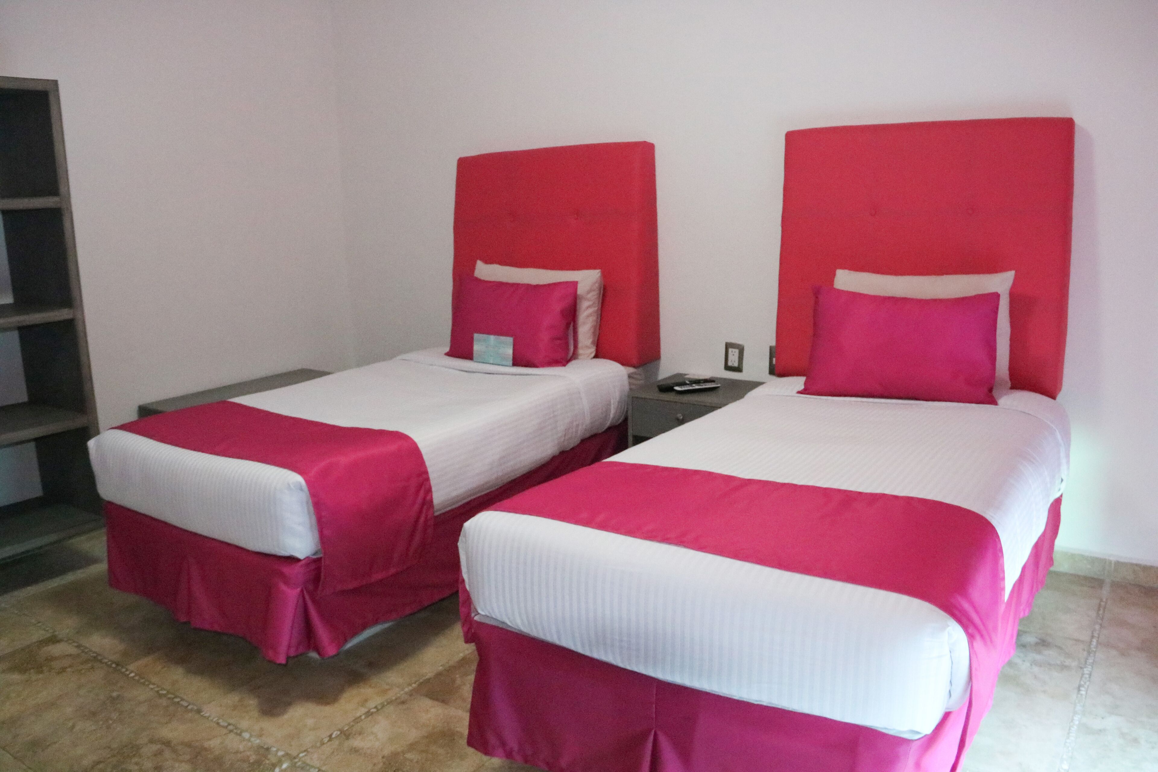 Two beds with red headboards and white bedding in a room with a tiled floor.