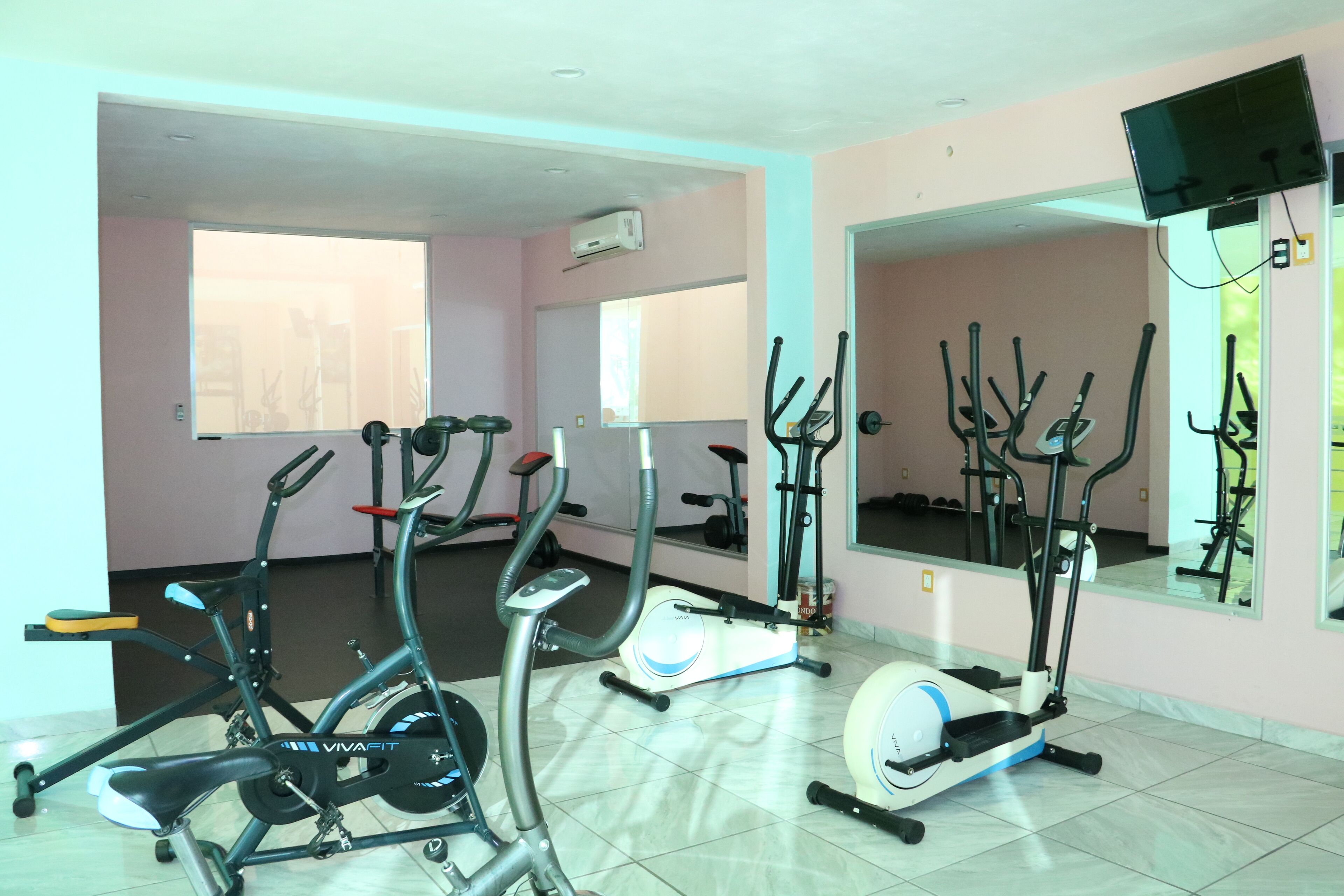 A gym with various exercise equipment, including treadmills and stationary bikes, in a room with large windows and a mirror.