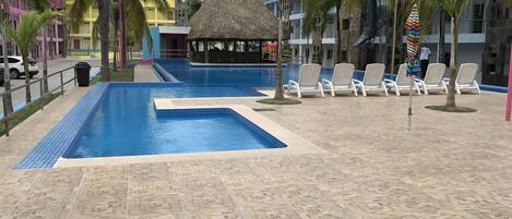 Un área de piscina con sillas de descanso y una estructura con techo de paja.