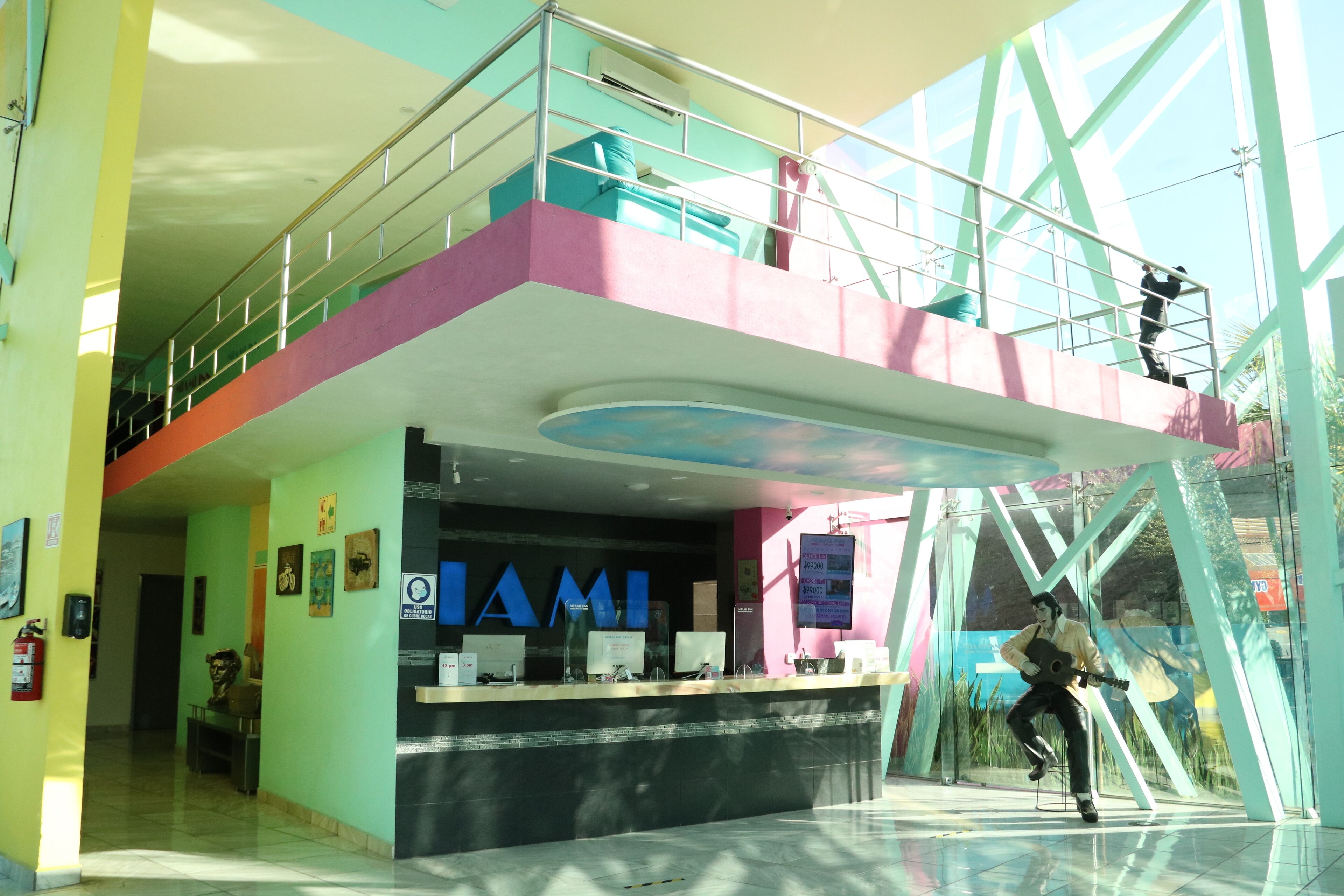 A brightly colored reception area with a prominent 'MIAMI' sign, a glass facade, and a person on a balcony.