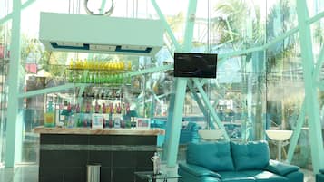 Un espace bar moderne avec un comptoir en verre, un téléviseur fixé au mur et un canapé de couleur turquoise.