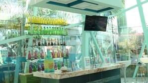 Zona bar moderna con una vetrina in vetro piena di bottiglie colorate, uno schermo televisivo e un bancone verde.