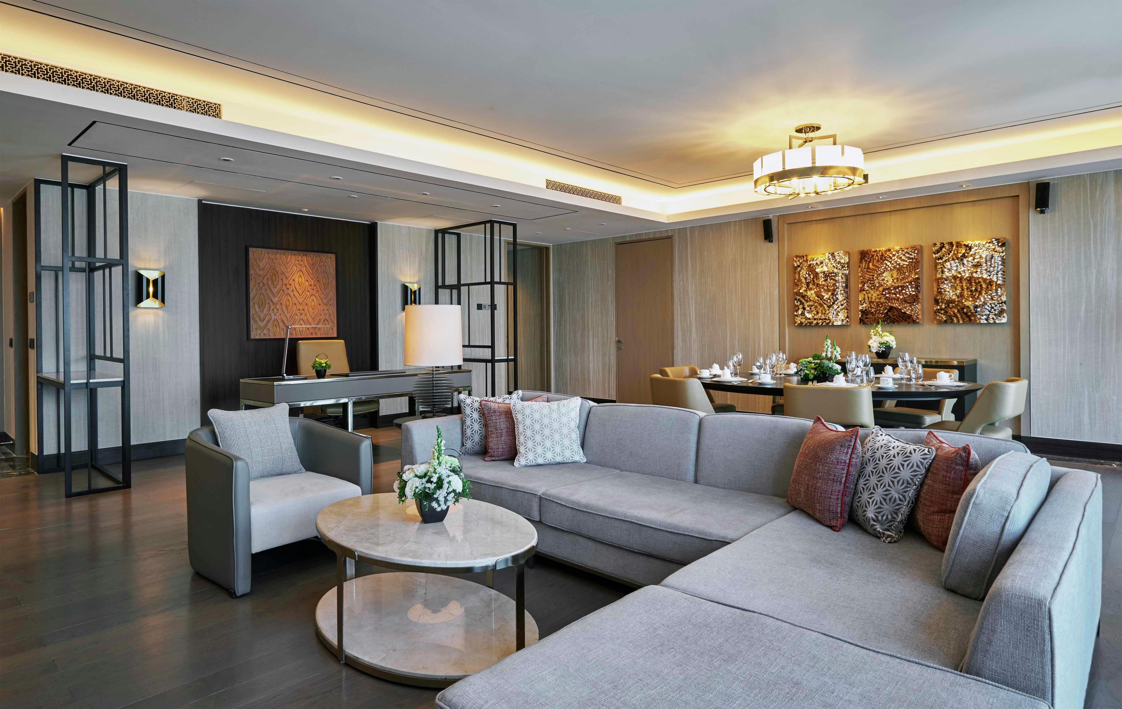 A modern living room with a sectional sofa, a round coffee table, and a dining area with a chandelier.