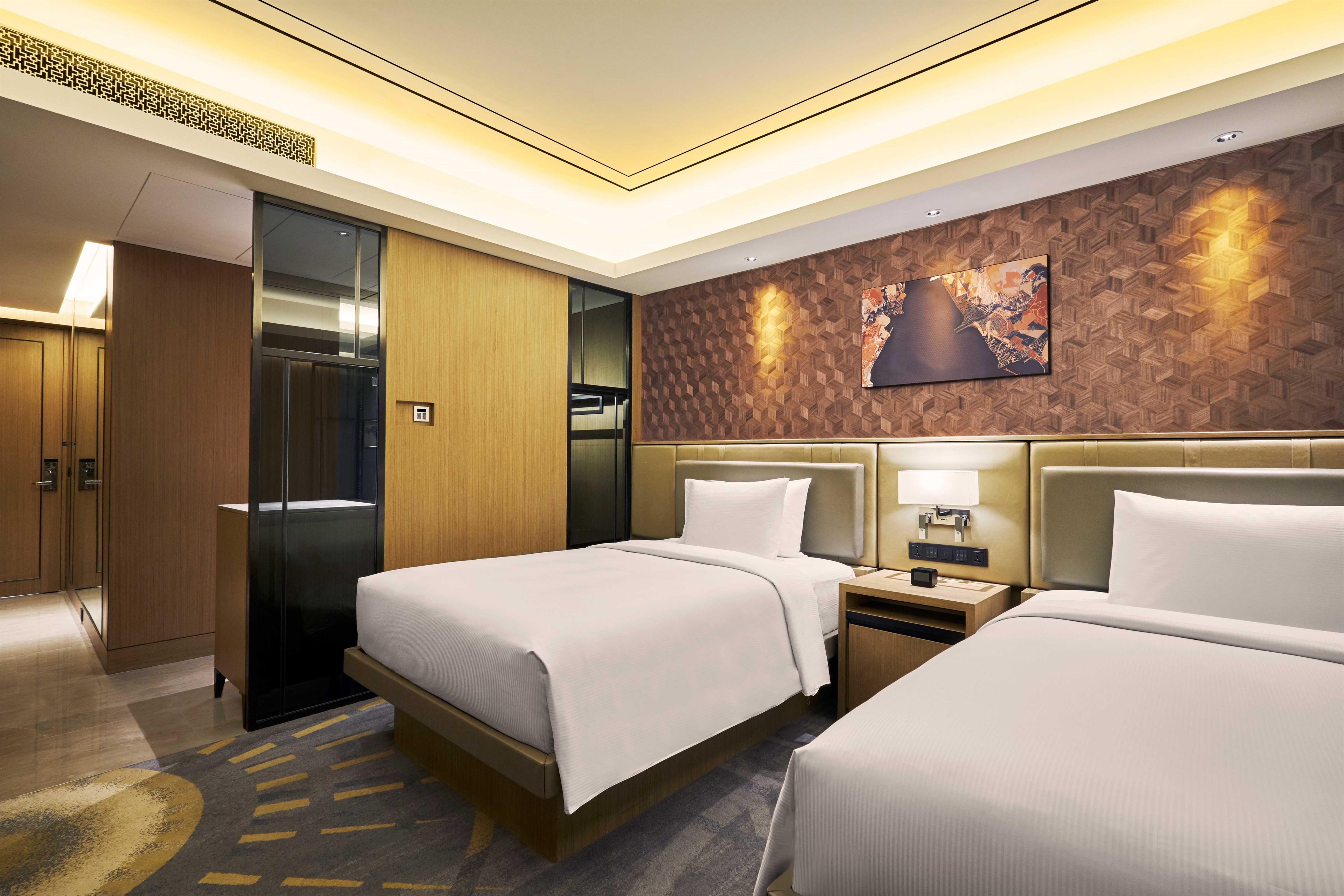 Une chambre d’hôtel avec deux lits, un grand miroir, un mur décoratif en bois et un tableau représentant un paysage urbain.
