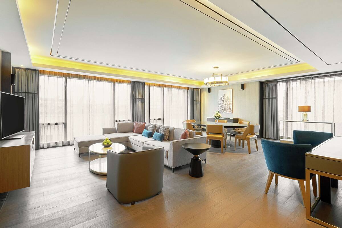A modern hotel room with a living area, dining space, and a TV.