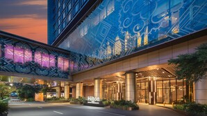 A modern hotel entrance with a large glass facade displaying geometric patterns, a well-lit lobby area, and the Hilton New York Midtown nameplate. - Hilton Manila Newport World Resorts (Pasay)