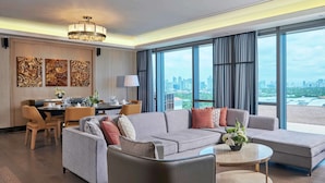 A modern hotel room with a grey sofa set, a dining area with a table and chairs, and large windows offering a city view. - Hilton Manila Newport World Resorts (Pasay)