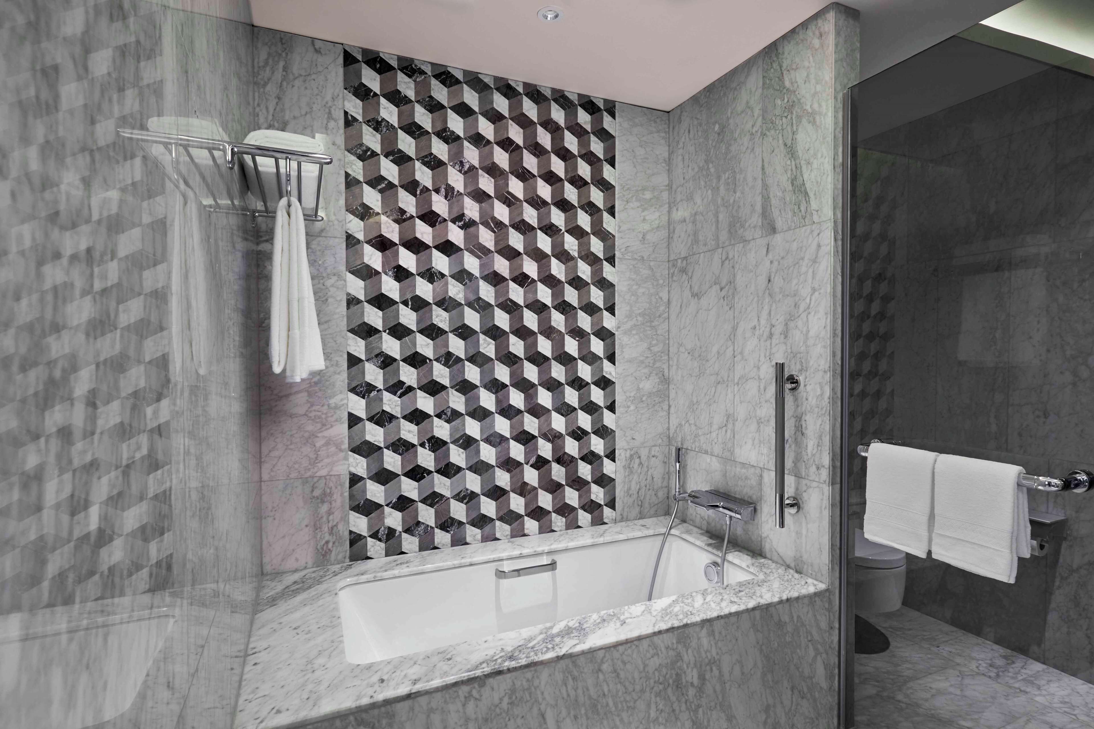 Un baño moderno con una pared de diseño geométrico, una bañera independiente y una zona de ducha con mampara de vidrio.