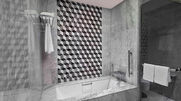 Un baño moderno con una pared de diseño geométrico, una bañera independiente y una zona de ducha con mampara de vidrio.