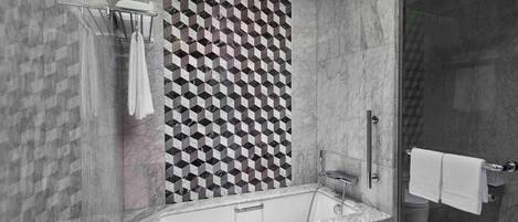 A modern bathroom with a geometric patterned wall, a freestanding bathtub, and a glass-enclosed shower area.
