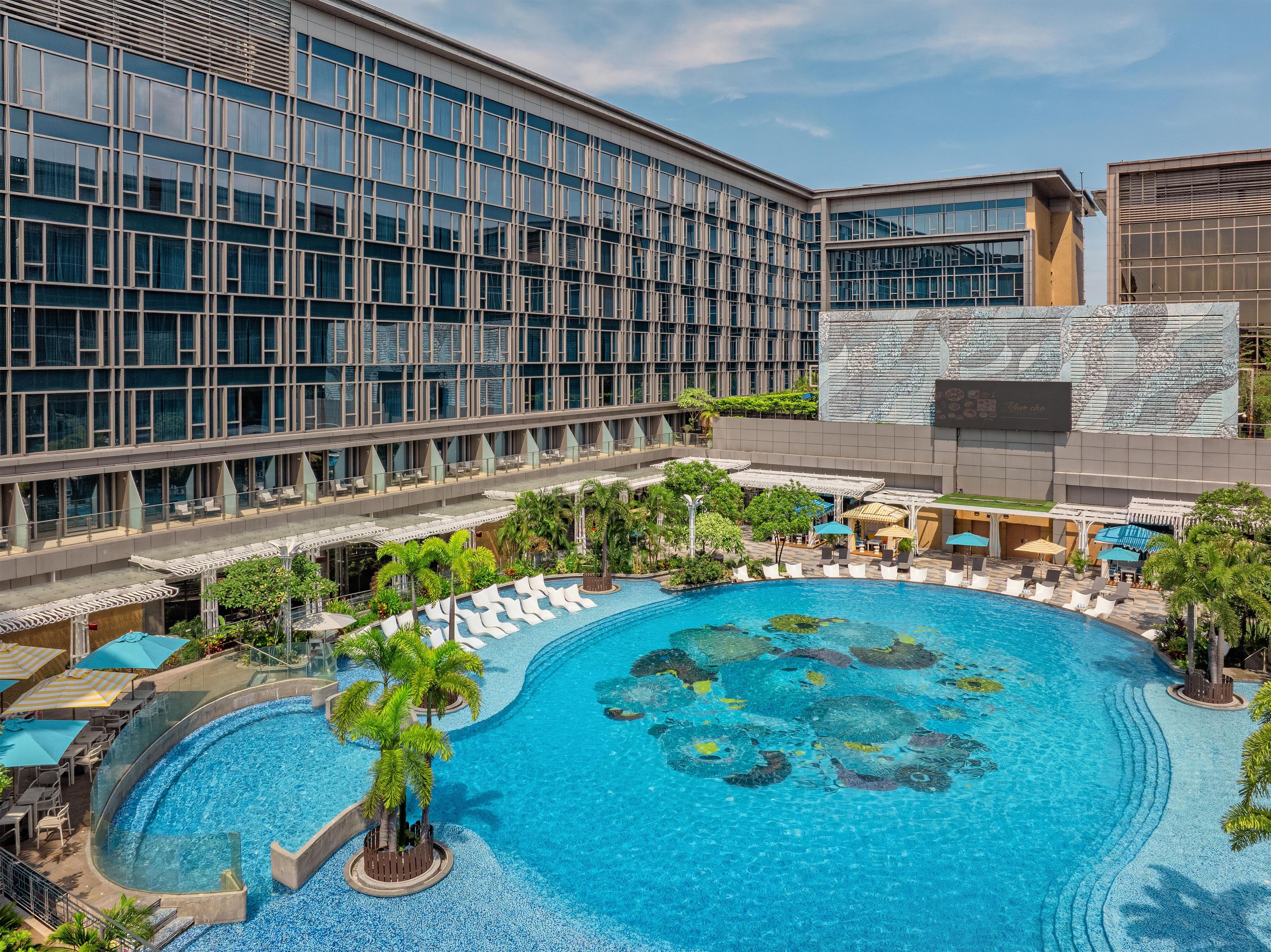 A hotel with a large swimming pool surrounded by lounge areas and palm trees.