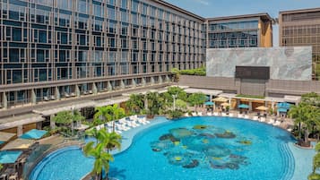 A hotel with a large swimming pool surrounded by lounge areas and palm trees.
