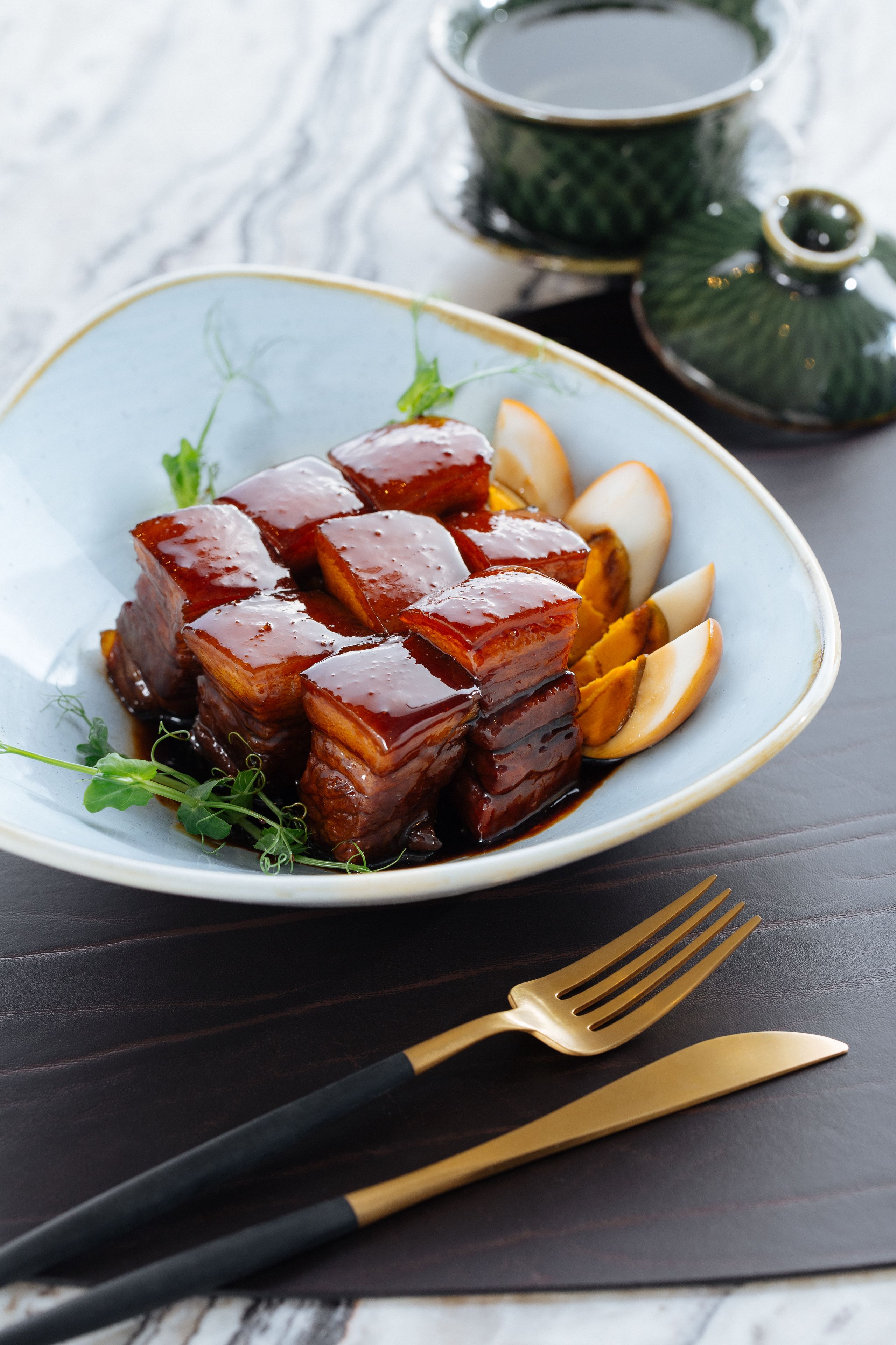 A plate of glazed pork belly with sliced apples and greens on a white plate.