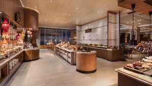 A modern hotel lobby with wooden flooring, a central bar area, and various food stations. - Hilton Manila Newport World Resorts (Pasay)