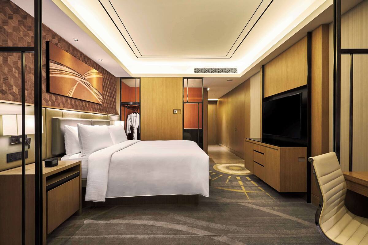 A hotel room with a bed, a TV, a seating area, and a wardrobe.